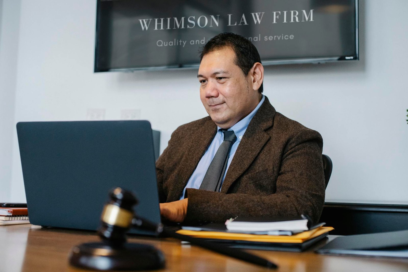 A lawyer working on a laptop in a legal office, wearing a suit and tie, with a gavel on the desk.